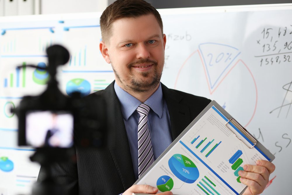Man in pak presenteert beleggingsgrafieken voor camera tijdens opname van videotutorial.