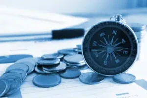 Kompas tussen stapeltjes munten symboliseert richting zoeken bij beleggen op de beurs