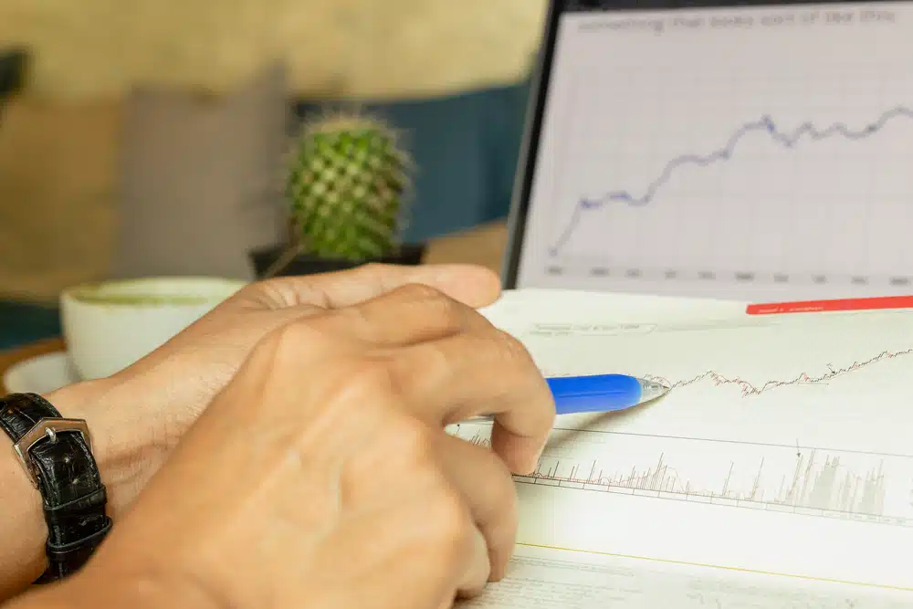 Hand die wijst naar een koersgrafiek in een boek ter ondersteuning van beleggen voor beginners